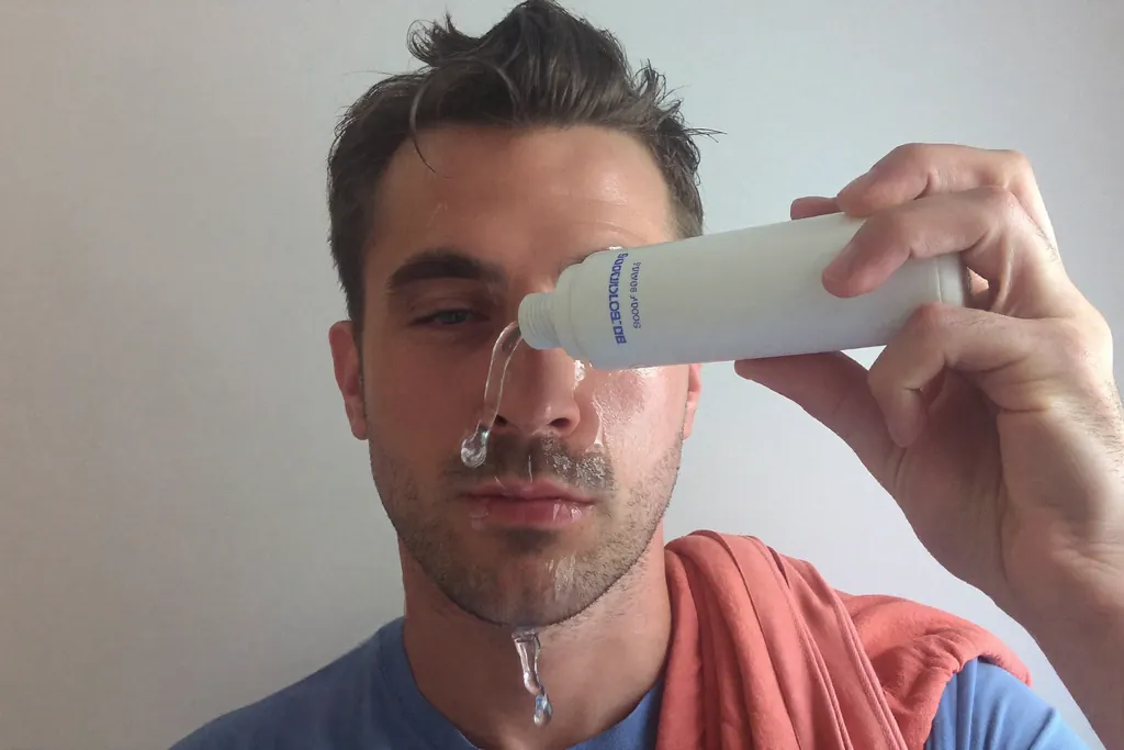 Hombre echándose agua en la cara en el lavamanos